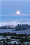Moon setting over the snowy Luss hills before sunrise in winter